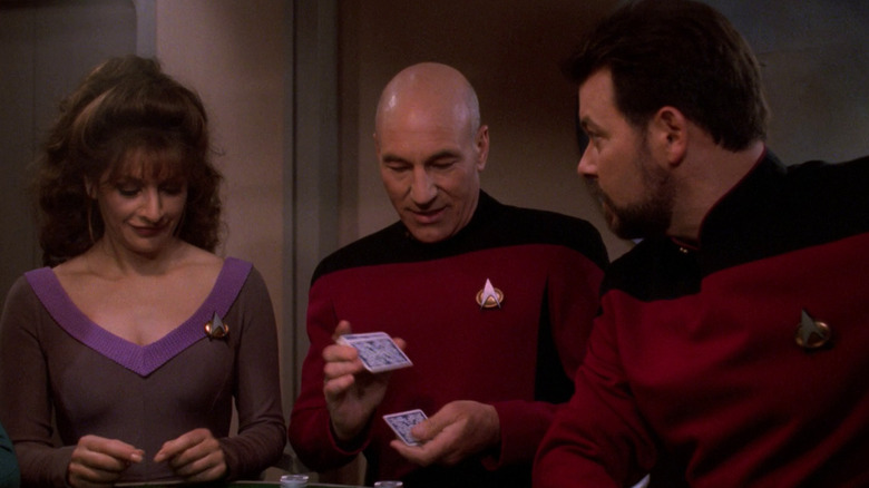 Picard shuffles cards at the poker table with Troi and Riker