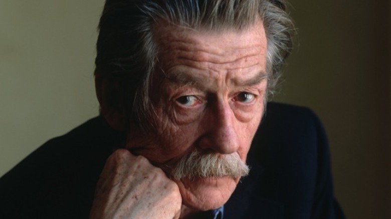 John Hurt looking at the camera with his head on his hand