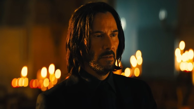 John Wick standing in front of several candles 