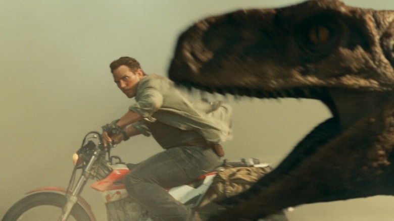 Owen drives motorcycle next to dinosaur