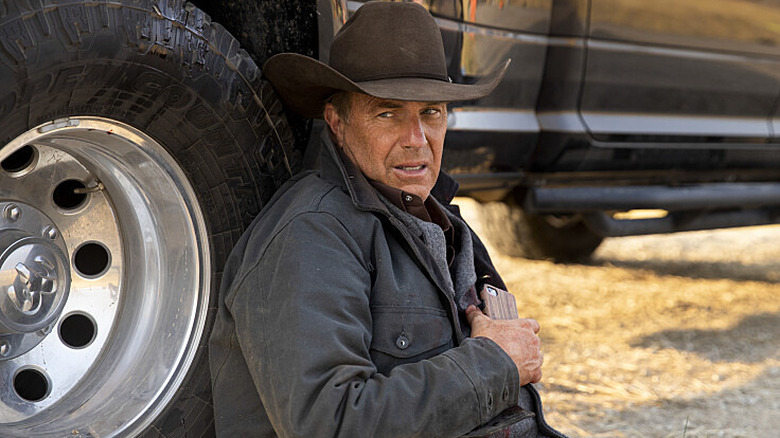 John Dutton from Yellowstone sitting next to car