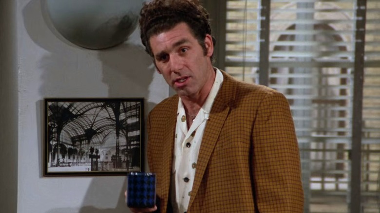 Kramer holding mug leaning against wall