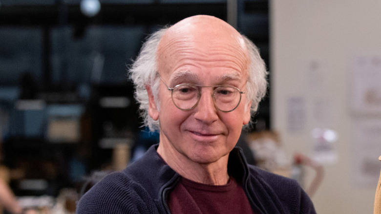 Larry David wearing a navy sweater and crimson shirt