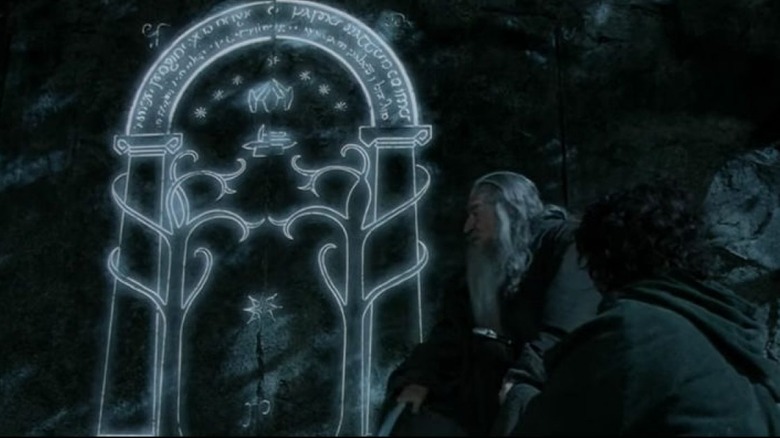 Gandalf and Frodo sit in front of the Doors of Durin