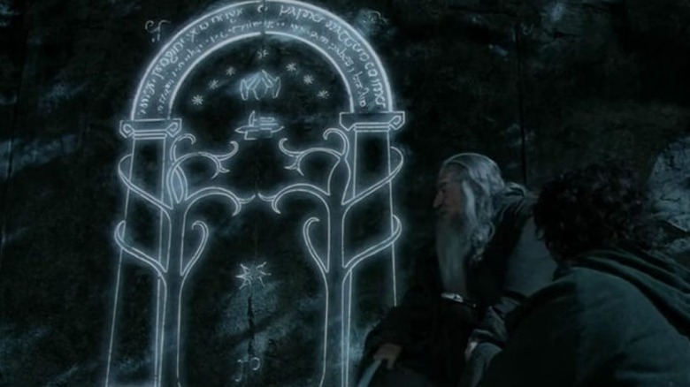 Gandalf and Frodo sit in front of the Doors of Durin