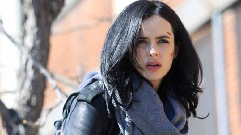 Jessica Jones squints wearing a scarf and leather jacket