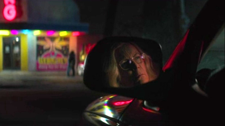 Laurie watches, her face reflected in a rear-view mirror