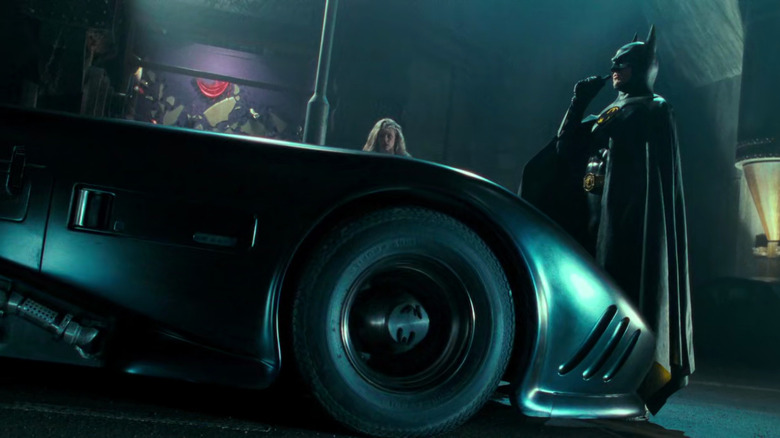 Batman stands next to Batmobile