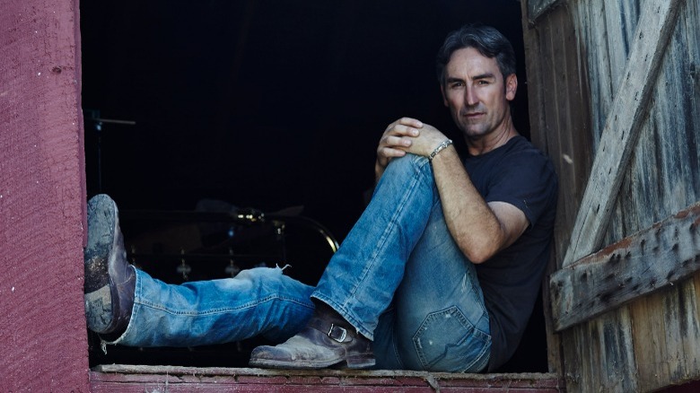 Mike Wolfe sitting in a barn, one leg bent