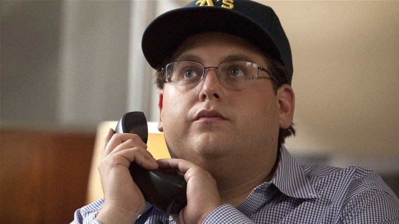 Peter Brand talking on the phone wearing an A's cap