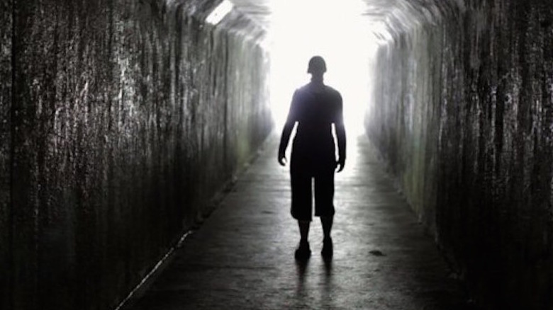 A dark figure is framed in light in a tunnel