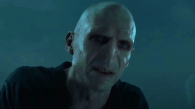 Voldemort stands over Harry to deliver a wicked threat.