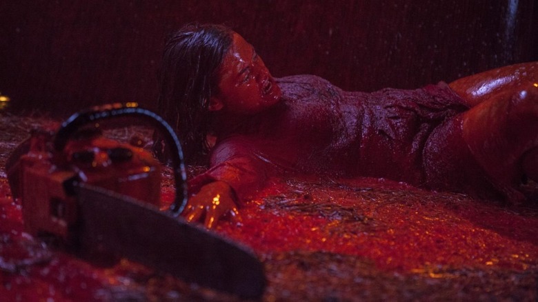 Woman covered in blood laying next to chainsaw 