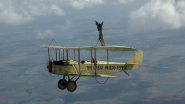 A stuntperson stands on a plane's wing