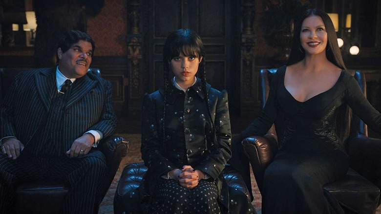 Gomez, Wednesday, and Morticia sit in chairs