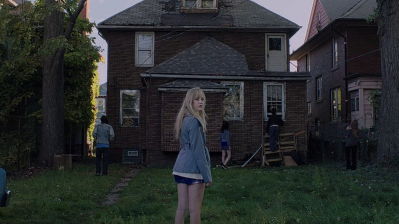 Maika Monroe stands in front of house