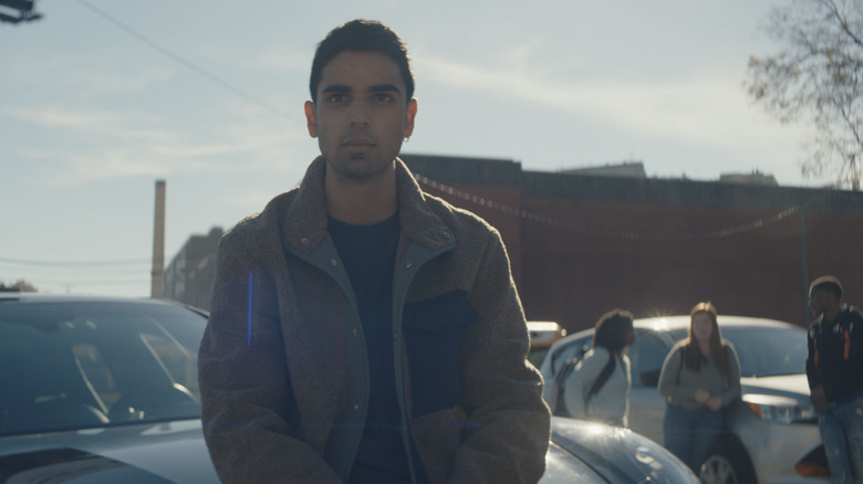 Kamran scowling next to line of cars