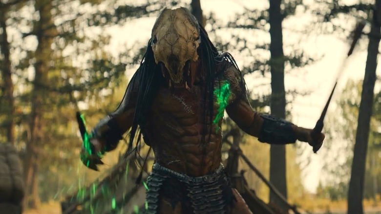 Predator with green blood holding weapons in its arms