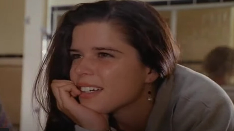 Neve Campbell watches someone in school hallway