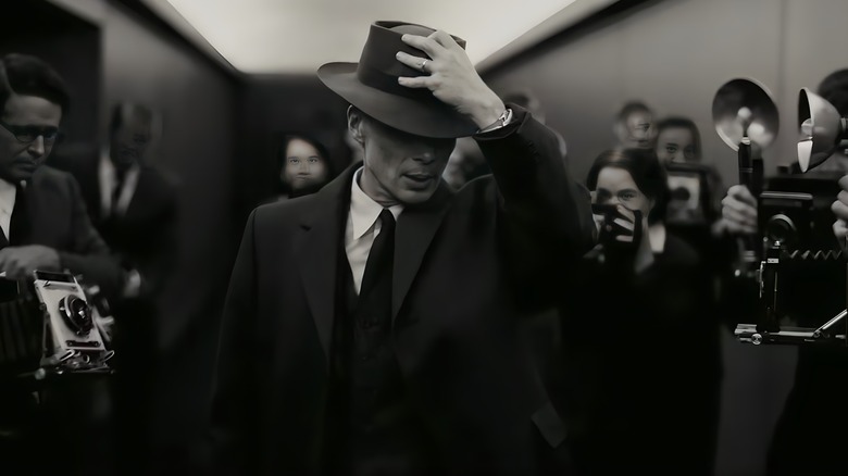 Oppenheimer holding his hat as he steps through crowd of photographers