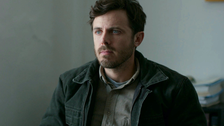 Casey Affleck sits by a white wall