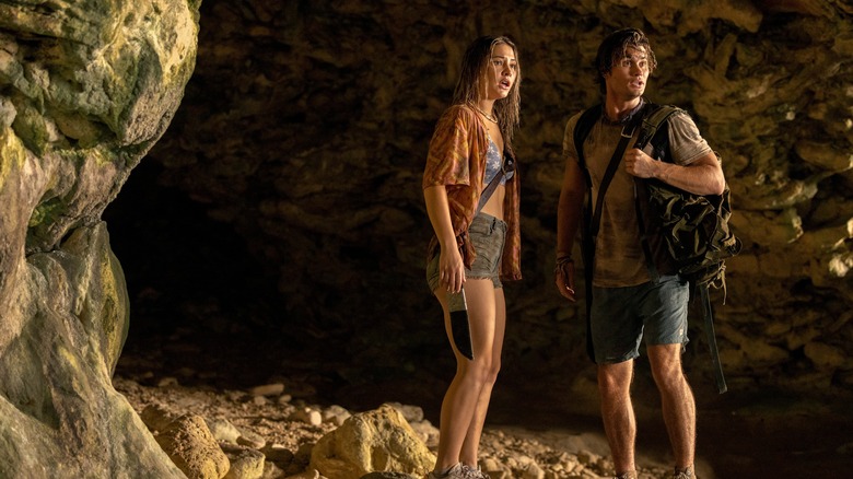 Chase Stokes and Madelyn Cline standing together outside cave