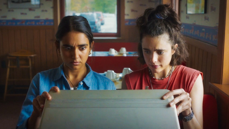 Geraldine Viswanathan and Margaret Qualley looking inside briefcase