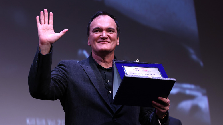 Quentin Tarantino waving to the crowd while holding an award