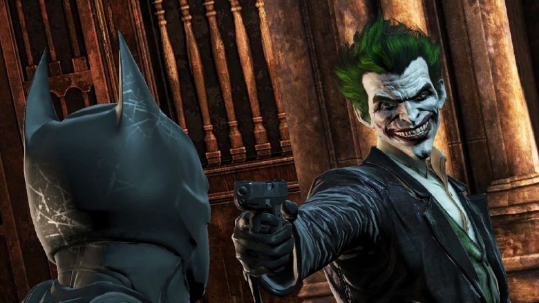 the joker points gun at Batman