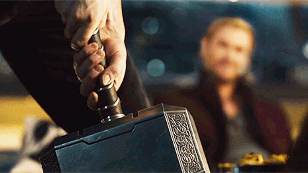 Chris Evans as Steve Rogers trying to lift Mjolnir while Thor (Chris Hemsworth) watches in the background in Avengers: Age of Ultron