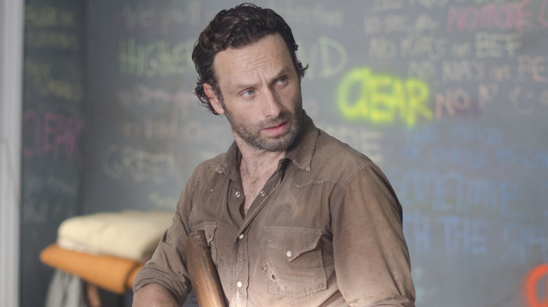 Rick holds gun in front of chalkboard