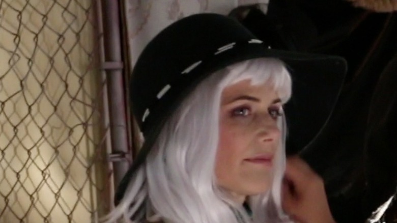 Sarah Clarke wears a hat and wig