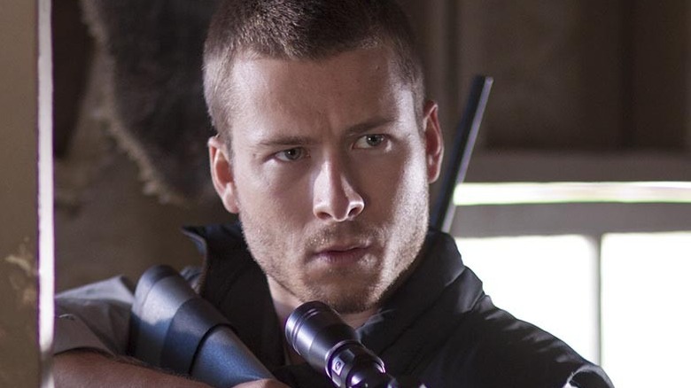 Glen Powell holds a rifle