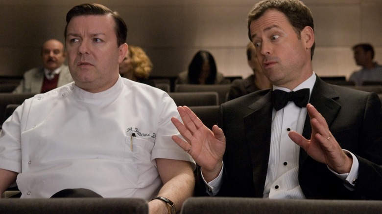 Concerned Ricky Gervais and Greg Kinnear with hands raised