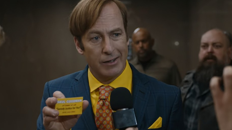 Saul Goodman gives a crooked smile holding his business card 