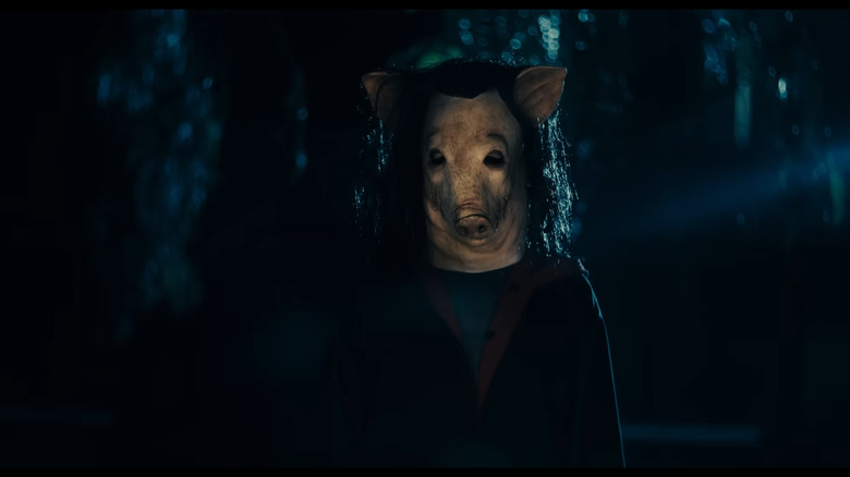 A person in a pig mask stands in the dark