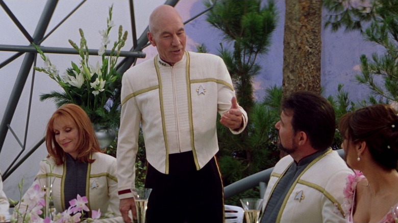 Picard speaks while his seated crew listens, smiling