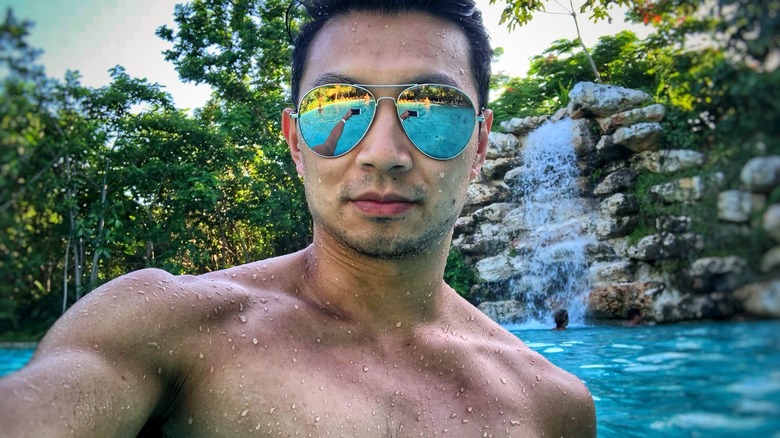 Simu Liu taking a shirtless selfie with sunglasses in a pool