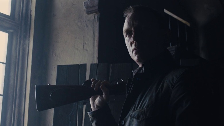 Bond holds a rifle over his shoulder near a window