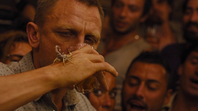 Bond takes a drink while looking at a scorpion on his hand