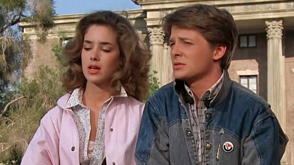Claudia Wells as Jennifer wears a pink jacket and sits next to Michael J Fox as Marty in his denim jacket with button in Back to the Future