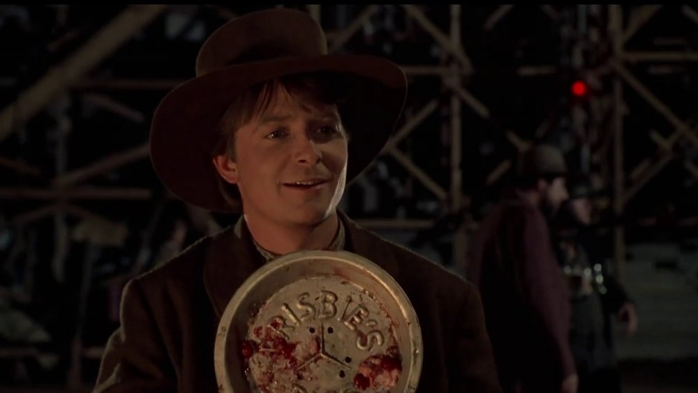 Michael J Fox as Marty McFly in Western gear laughingly holds up a pie dish engraved with Frisbie's Pies in Back to the Future III