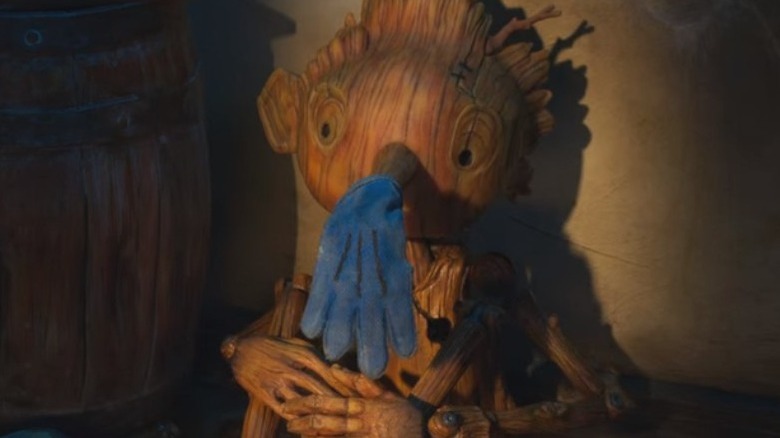 Pinocchio sits with blue glove on his nose