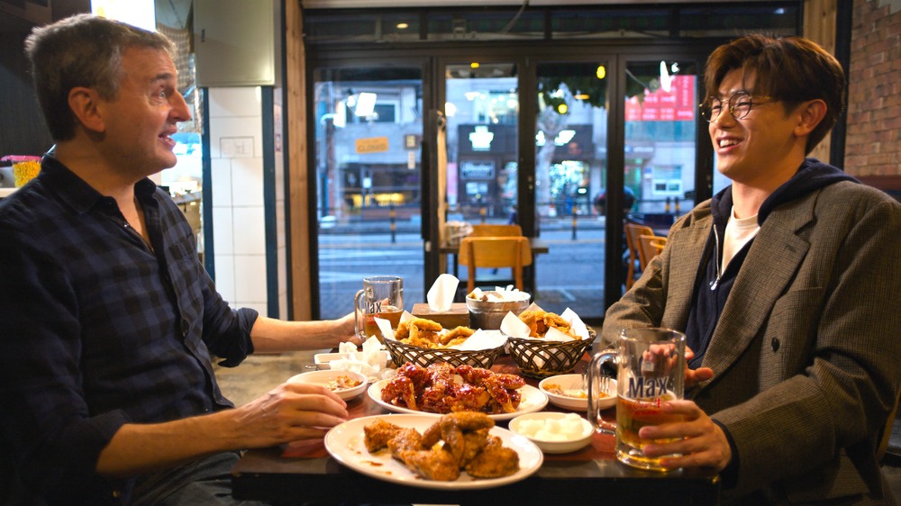 Phil Rosenthal and Eric Nam talking with beer and wings on table