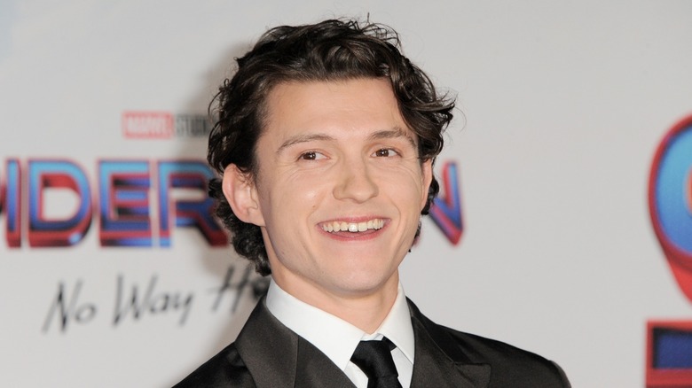 Tom Holland smiling in front of Spider-Man logo