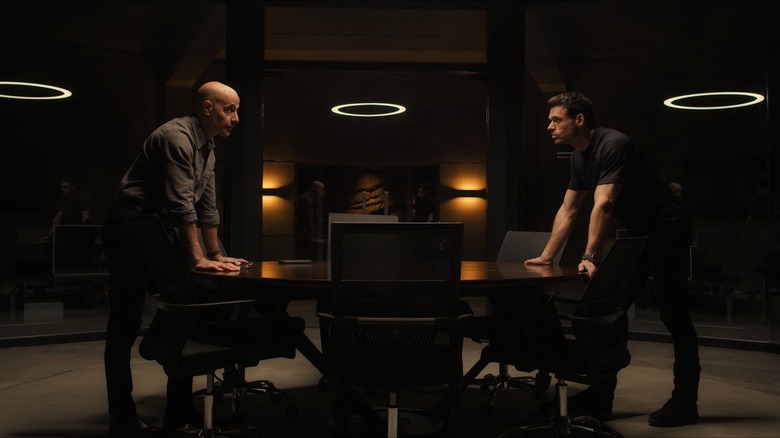 Bernard and Mason leaning over opposite sides of table in "Citadel"