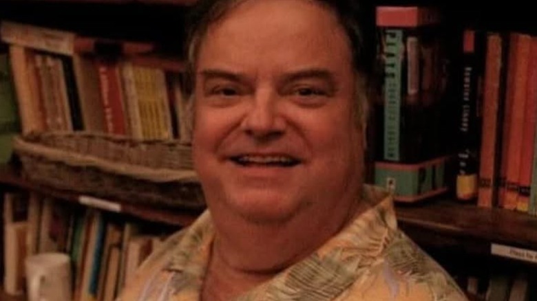 Robert Machray smiling in front of bookshelves