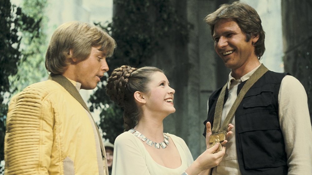 Carrie Fisher as Princess Leia gives Harrison Ford as Han Solo a medal as Mark Hamill as Luke Skywalker looks on in Star Wars: A New Hope