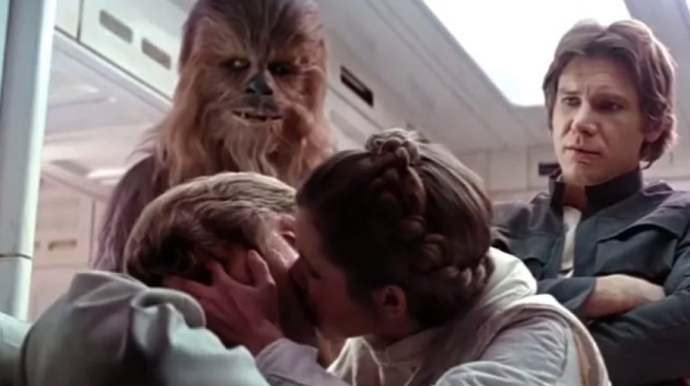 Carrie Fisher as Princess Leia kisses Mark Hamill as Luke Skywalker as Chewie and Harrison Ford as Han Solo look on