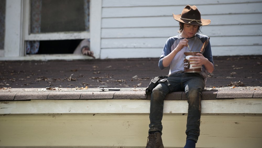 Chandler Riggs sitting on a roof eating pudding from a giant can in The Walking Dead